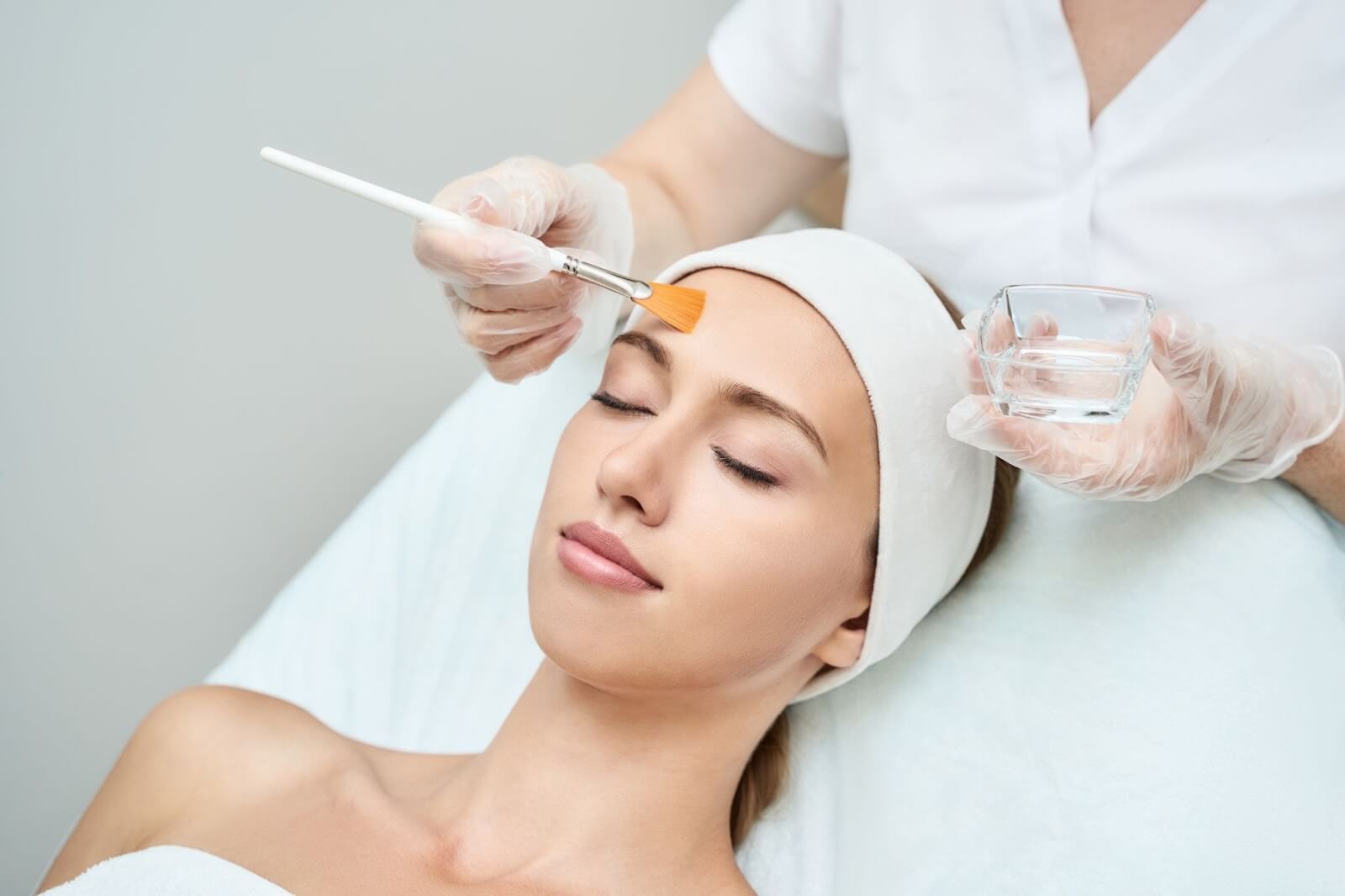 A clinician applying a chemical peel solution to a patient’s face